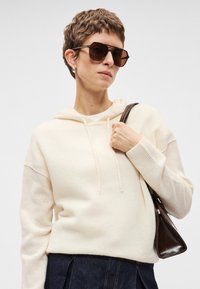 Κρέμ χρώματος φούτερ με κουκούλα, κατασκευασμένο από μαλακό υλικό, με χαλαρή εφαρμογή, ριμπ μανσέτες και λεπτή υφή. Σκοτεινή τσάντα στον ώμο.