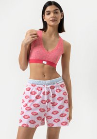 Růžový krajkový bralette s výstřihem do V a elastickým pásem, doplněný bílými šortkami s potiskem červených rtů a světle modrým elastickým pasem.