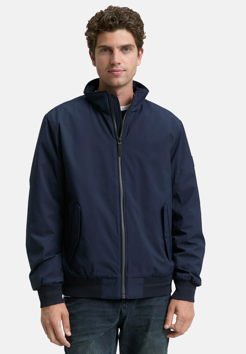 Marineblaue Bomberjacke aus glattem Stoff mit Stehkragen, Reißverschluss und seitlichen Taschen. Mit gerippten Bündchen und Saum.