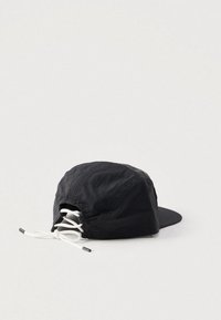 Fekete sapka enyhén texturált anyagból, hajlított napellenzővel és fehér, hátul méretállításra szolgáló állítható zsinórokkal.