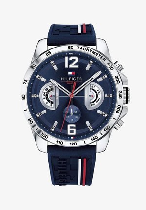 Zegarek Tommy Hilfiger z granatowym gumowym paskiem i srebrną kopertą. Posiada niebieską tarczę, białe znaczniki godzin, czerwone akcenty oraz skalę tachymetryczną.