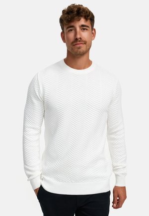 Hvid sweater med et struktureret fiskebensmønster, ribbet halsudskæring og manchetter, parret med mørke bukser. Renset, minimalistisk design.