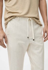 Light beige drawstring pants with vertical stripes, crafted from soft fabric. Features contrast hardware accents and an adjustable waistband.