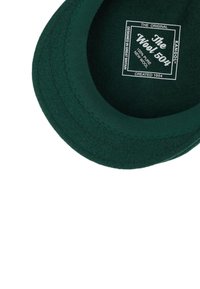 Beret de lana verde con forma redonda. Presenta una etiqueta cosida en el interior que muestra detalles de la marca y del material. Textura suave, diseño clásico.