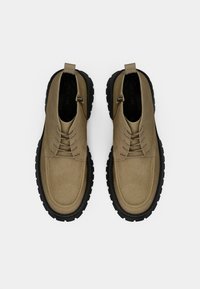 Tan odiniai batai su elastingais raiščiais, apvaliu pirštu ir tvirtu juodu guminėm padu. Įeina užpakalinė kilpa patogiam užsidėjimui.