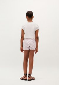 Top blanco de manga corta, pantalones cortos rosa claro con patrón de leopardo y sandalias negras con tiras. Vista desde la parte posterior sobre un fondo neutral.
