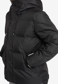 Musta toppatakki, jossa vetoketjulla suljettava etuosa, huppu ja sivutaskut. Takissa on sileä pinta ja taskussa näkyy brändilogot "FORAFEW".