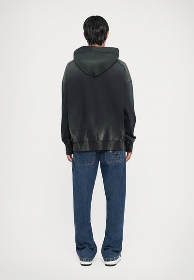 Fekete, átmenetes hatású kapucnis pulóver, bő kék farmernadrággal, amelyen varrási részletek és hátsó zsebek találhatók.