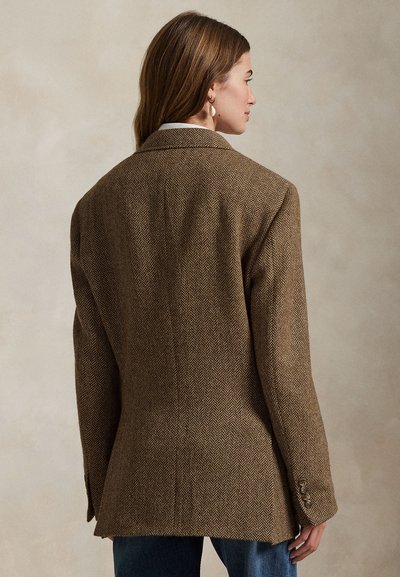 Brązowa marynarka jodełka z wyraźnie zarysowanymi ramionami i pojedynczym zapięciem na guzik, z długimi rękawami i dopasowanym krojem.
