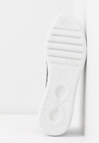 Semelle en caoutchouc blanc avec texture en creux, arborant un logo et un motif floral. Matière supérieure sombre visible au talon.