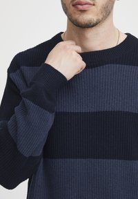 Pulover cu dungi bleu marin, având un design tricotat texturat cu dungi întunecate și deschise contrastante; manșete și guler în relief.