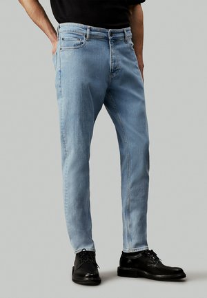 Jeans in denim azzurro chiaro con vestibilità slim, design a cinque tasche e cuciture a contrasto, abbinati a scarpe eleganti in pelle nere.