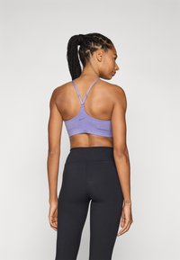 Top desportivo roxo com alças ajustáveis, apresentando um acabamento texturizado e o logótipo da Nike. Combinado com leggings pretas de cintura alta.