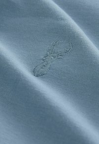 Light blue fabric showing a close-up of a stitched lobster motif. The texture is smooth with a fine knit pattern.