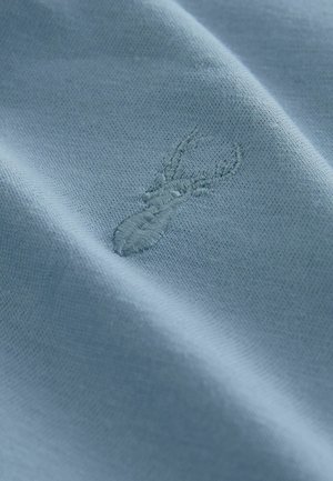 Svetlo modro blago prikazuje bližnji posnetek šivane rakovice. Tekstura je gladka z drobnim pletenim vzorcem.