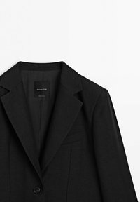 Zwarte getailleerde blazer met reverskraag met insnijding, enkele knoopsluiting en borstzak met bies, met label Massimo Dutti, op witte achtergrond.