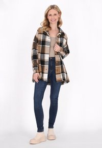 Rutig overskjorta i brunt, svart och vitt, med knappstängning framtill och en avslappnad passform, kombinerad med mörka jeans och beigefärgade platåstövlar.