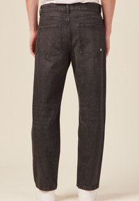 Pantalones de mezclilla negros con un corte relajado, que cuentan con dos bolsillos traseros y una pierna ajustada. El material tiene una apariencia texturizada y desgastada.