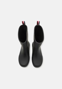 Bottes en caoutchouc noires avec une texture lisse, un design haut et une sangle à tirer rouge, blanche et bleue à l'arrière.