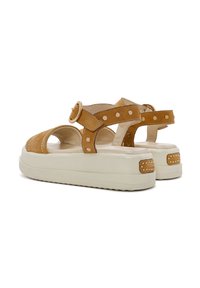 Sandali platform in pelle color tan con ritagli circolari, dettagli in borchie sulle cinghie e una suola spessa di color crema. Accentati da fibbie rotonde.