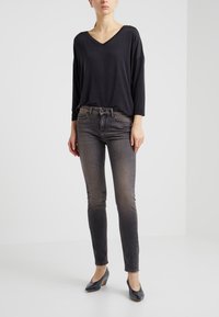 Top negro de corte holgado con escote en V y mangas largas, combinado con jeans ajustados oscuros y deslavados, además de zapatos de tacón negros. Diseño simple y textura suave.