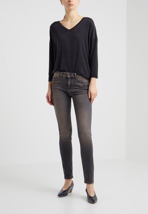 Top negro de corte holgado con escote en V y mangas largas, combinado con jeans ajustados oscuros y deslavados, además de zapatos de tacón negros. Diseño simple y textura suave.