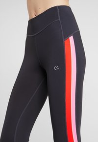 Leggings neri a vita alta con strisce verticali contrastanti in rosso e rosa. Presentano una texture morbida e un logo discreto sulla coscia.