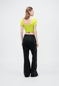 Pulover scurt de culoare verde lime, dintr-un material texturat, cu mâneci scurte, asortat cu pantaloni negri evazați, cu dungi albe pe laterale.