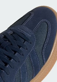 Scarpa sportiva blu navy caratterizzata da un mix di camoscio e tessuto testurizzato, con suola in gomma naturale e lacci a vista. Finiture in cucitura sui dettagli.