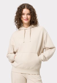Beige hoodie met een voorzak, een capuchon met trekkoord en ribgebreide manchetten. Zachte textuur en een relaxte pasvorm. Gecombineerd met bijpassende broek.