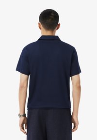 Marinblå pikétröja med en mjuk textur, korta ärmar och krage; har en rak nederkant och minimalistisk design.