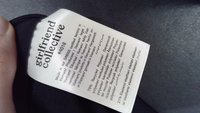 Svart stofflabel med merkevaren "girlfriend collective". Inneholder vedlikeholdsinstruksjoner på flere språk, angir 79 % resirkulert polyester, 21 % elastan.