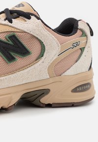 Baskets New Balance 530 beige et rose avec logo noir, accents verts, texture suédée et semelle amortissante ABZORB, vues de profil.