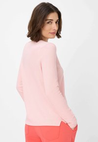 Langärmliges, geripptes pinkes Oberteil mit Rundhalsausschnitt, seitlichen Schlitzen am Saum und taillierter Passform. Getragen mit korallenfarbenen Hosen.