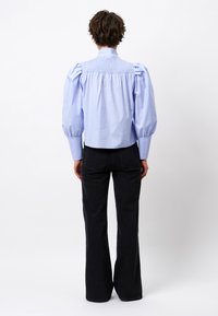 Light blue shirt with puffed sleeves, smocked back, and a spread collar, paired with black flared pants. Textured cotton fabric.