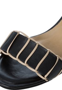 Sandalo nero con una larga fascia e dettagli in camoscio color tan, realizzato in pelle liscia. Il design include una punta arrotondata e un tallone aperto.