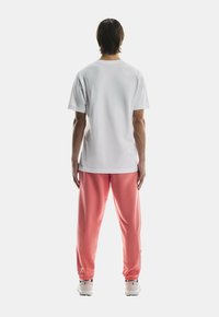 Vit bomull t-shirt med korta ärmar, kombinerad med rosa sweatpants med elastiska muddar och en logotyp nära fållen. Neutral bakgrund.