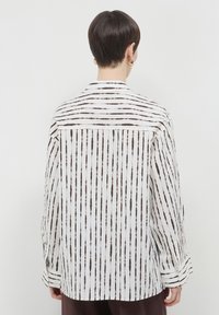 Camicia maniche lunghe in tessuto bianco con righe verticali marroni. Presenta un colletto con bottoni e un bacino sul retro. Vestibilità regolare con maniche con polsini.
