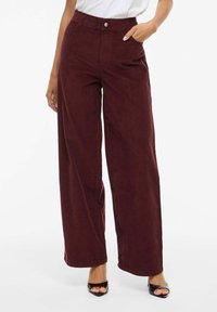 Wijd uitlopende bordeauxrode ribfluwelen broek met hoge taille, riemlussen, zijzakken en een knoopsluiting aan de voorkant; gladde textuur met een lichte glans.