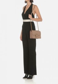 Combinaison noire avec un décolleté en V profond et une ceinture blanche, associée à un sac à main beige avec des accents en matériel doré et une chaîne.