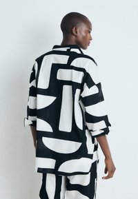 Camisa de patrón en blanco y negro con formas abstractas audaces. Hecha de tela ligera, tiene un corte relajado y mangas enrolladas.