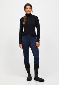 Maglietta nera a maniche lunghe con mezza zip, leggings blu navy con dettagli neri e logo, abbinati a comode calzature nere e calze grigie. Tessuto morbido.
