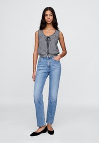 Svart-hvitt rutete ermeløs topp med rysjekant, kombinert med lyseblå høytlivede, rette jeans og svarte flate sko.