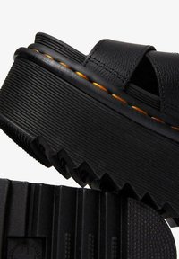 Sandalias de plataforma negras con una suela de goma texturizada, parte superior de sintético suave y un detalle de costura anaranjada en contraste a lo largo del borde.