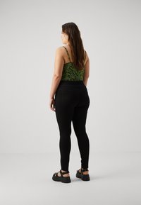 Black denim leggings with a high waist and back pockets, paired with a green zebra print tank top. Model has long brown hair and black sandals.