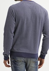 Jersey de mezcla de algodón en azul marino con tejido texturizado, mangas raglán, puños y cintura acanalados; vista trasera que muestra un detalle mínimo de costuras.