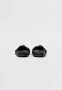 Black slide sandals with a soft, textured upper, open toe design, and flat rubber sole, featuring a minimalist aesthetic.