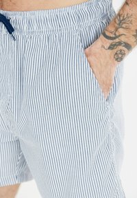 Randiga badshorts i ljusblått och vitt, med dragsko i midjan och sidofickor, tillverkade av ett mjukt och lätt tyg.