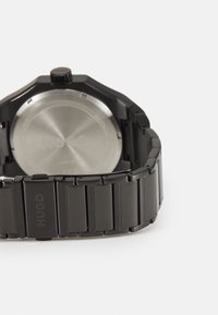 Black metal wristwatch with an octagonal case, a polished stainless steel back, and a segmented link bracelet displaying the brand name "HUGO."