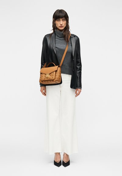 Sac à main marron avec fini texturé, garnitures dorées, bandoulière portée en travers, assorti à un col roulé gris et un blazer en cuir noir sur un pantalon blanc.